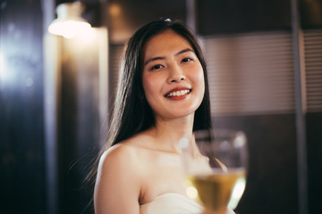 portrait of attractive young beautiful Asian woman holding glasses of wine or beer alcohol toasting to thcamera, focus on female happy smile face, lifestyle party music with light at night on rooftop 