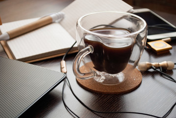  office table with cup of coffee behind wooden table with planners, stationery and laptop .   Glass cup in the shape of a heart and double glass in female hands.