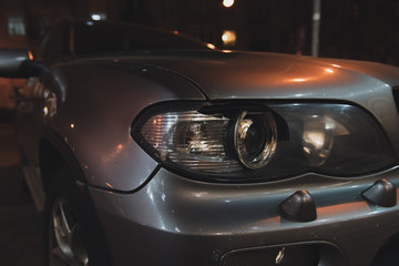 Grey car with broken headlight after a crash accident. Car on the street at night. Side view. Closeup.