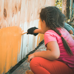 Repair in the home. Happy child girl paints the wall with yellow paint