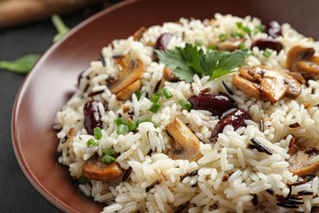 Delicious rice pilaf with mushrooms and beans in plate, closeup