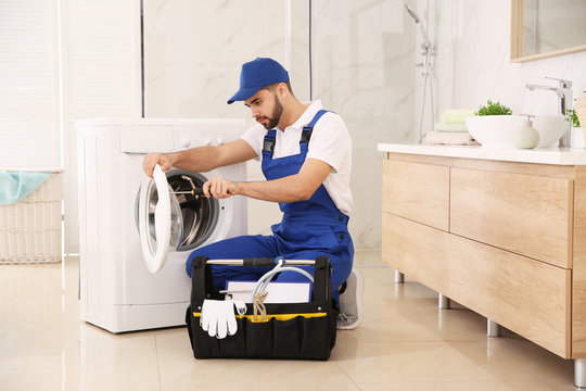 Professional plumber repairing washing machine in bathroom