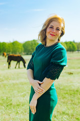 . Spring, trees are blooming, grass is growing . .woman walks on a background of a horse. woman dressed in a green fuck, office.