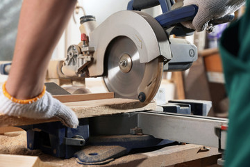 Professional carpenter cutting wooden planks with sawmill in workshop, closeup