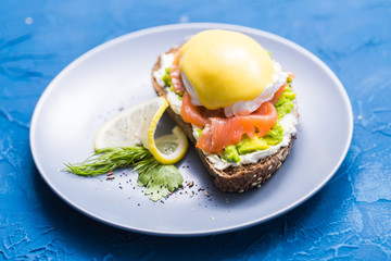 Sandwich with smoked salmon, egg and avocado on blue background. Concept for healthy nutrition.