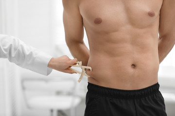 Nutritionist measuring man's body fat layer with caliper on blurred background, closeup