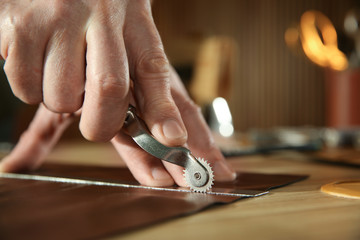 Man marking leather with roller in workshop, closeup