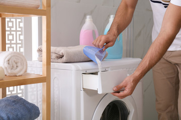 Man pouring laundry detergent into washing machine drawer in bathroom, closeup