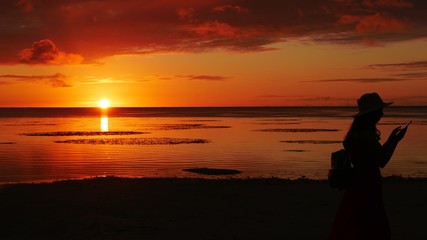 Fiery sunset in the sea with the silhouette of a woman taking photos with her phone