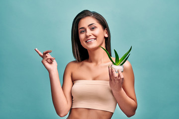 Skin care concept.Beautiful latin woman holding aloe leaves and cream in studio on blue background.