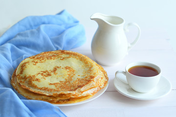 Pancake week: thin pancakes with jug and tea on white table.french crepes .thin pancakes and glass of milk on the table.Delicious breakfast.Selective focus