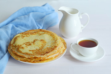 Pancake week: thin pancakes with jug and tea on white table.french crepes .thin pancakes and glass of milk on the table.Delicious breakfast.Selective focus