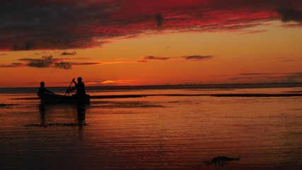 Wide shot with the silhouette of two boaters in the sea with dramatic sunset background