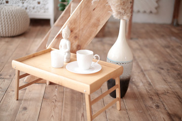 Breakfast set close up in the room. Coffee cup on a tray with statuette decoration. Selective focus. Boho style