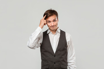 Young man in a white shirt and grey vest pointing with finger at the head
