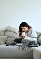 The young girl drinks tea on a gray sofa