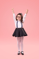 Excited little schoolgirl with raised hands on pink background