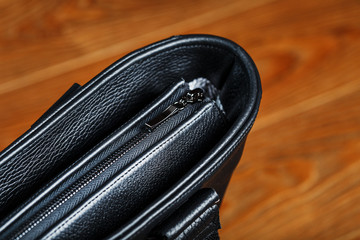 Handmade black leather bag on a wooden background, made of natural material.