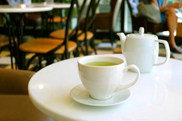 Closeup a cup of green tea and teapot on white round table in a tearoom