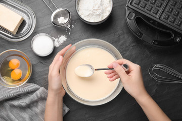Woman preparing dough for Belgian waffles at black table, top view