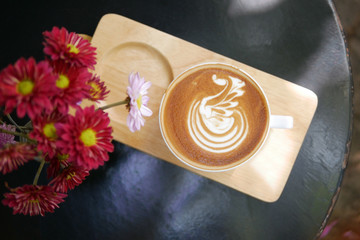 Hot coffee cappuccino latte art swan bird foam on wooden plate with flowers top view background
