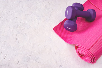 Two purple 1,5 kg dumbbells on pink fitness mat, white textured background. Gym, sports, fitness, training concept. Copy space for your text.