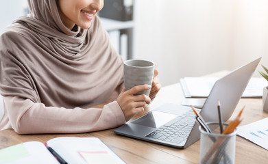 Muslim Woman Drinking Coffee At Desk And Working On Laptop