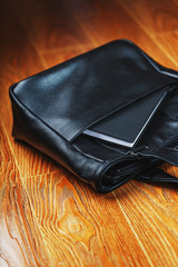 Black notebook peeking out of the pocket of a black leather bag close-up, macro Handmade, natural materials.