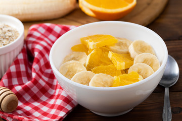 Bowl of oatmeal porridge with banana and orange  on wooden background, copy space