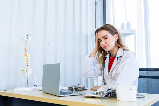 Stressed female doctor with stethoscope have headache working with laptop computer on wooden table in Hospital background