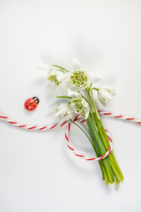 Bouquet of delicate snowdrops on white background with red and white string. First of march celebration Martisor concept. Soft focus, copy space, close up.