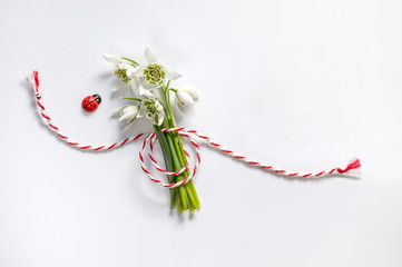Bouquet of delicate snowdrops on white background with red and white rope. First of march...