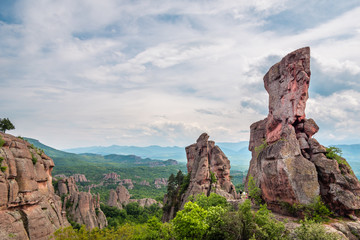 Landscape with bizarre rock formations, green mountain valley and cloudy sky in the background,...