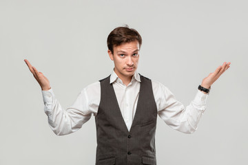Young man in a white shirt and grey vest shrugging his shoulders expressing emotion of confusion.