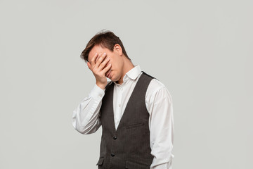 Handsome man in a white shirt and grey vest clutches head because he faces some problems.