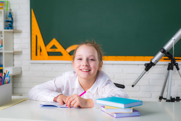 Girl with happy face expression near desk with school supplies.