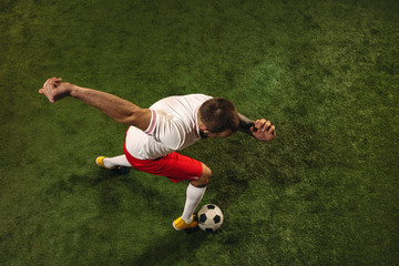 Top view of caucasian football or soccer player on green background of grass. Young male sportive model training, practicing. Kicking ball, attacking, catching. Concept of sport, competition, winning.