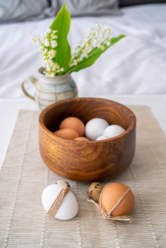Easter concept. Easter decoration with unpainted hens and quail eggs and wooden bowl on a textured mat.