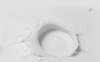 Fresh milk pouring making a crown splash in a milk pool. Top view, isolated on grey-white background.