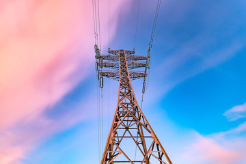 High voltage electricity pylons and transmission power lines on the blue sky background at sunset.