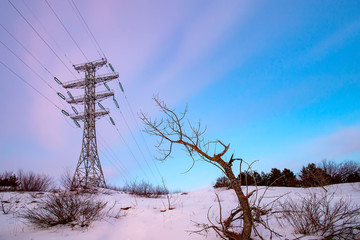 High voltage electricity pylons and transmission power lines on the blue sky background at sunset.