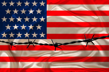 iron barbed wire against the background of the national silk flag of the USA state, concept of...