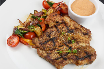 Grilled pork steak with sauce and vegetable on white plate