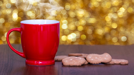 Red mug with hot tea and cookies on table on gold background with bokeh_