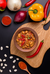 Macedonian bean dish Tavche graver on a wooden board next to the ingredients on a black background. vertical photo
