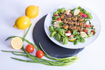 vegetables and a plate of prepared shrimp on sticks stands on a black tray on the table