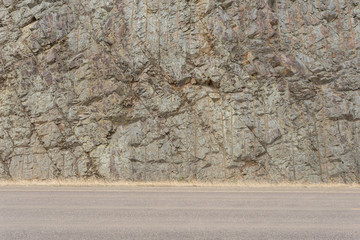Side of rock mountain alongside empty roadway