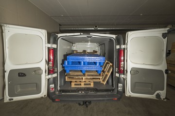 View of open white vehicle loaded with wooden and plastic pallets. 