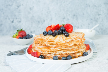 A stack of crepes lies in a plate, decorated with berries on a gray concrete background. Top view, copy of space.