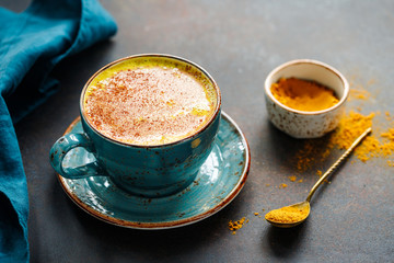 Closeup view of turmeric latte cup on a textured dark background. - 324301458